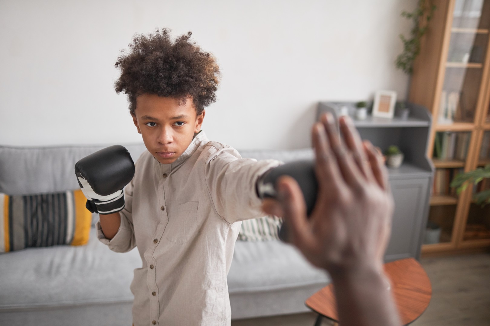Medium portrait shot of serious African American boy wearing boxing gloves training punches with his father at home