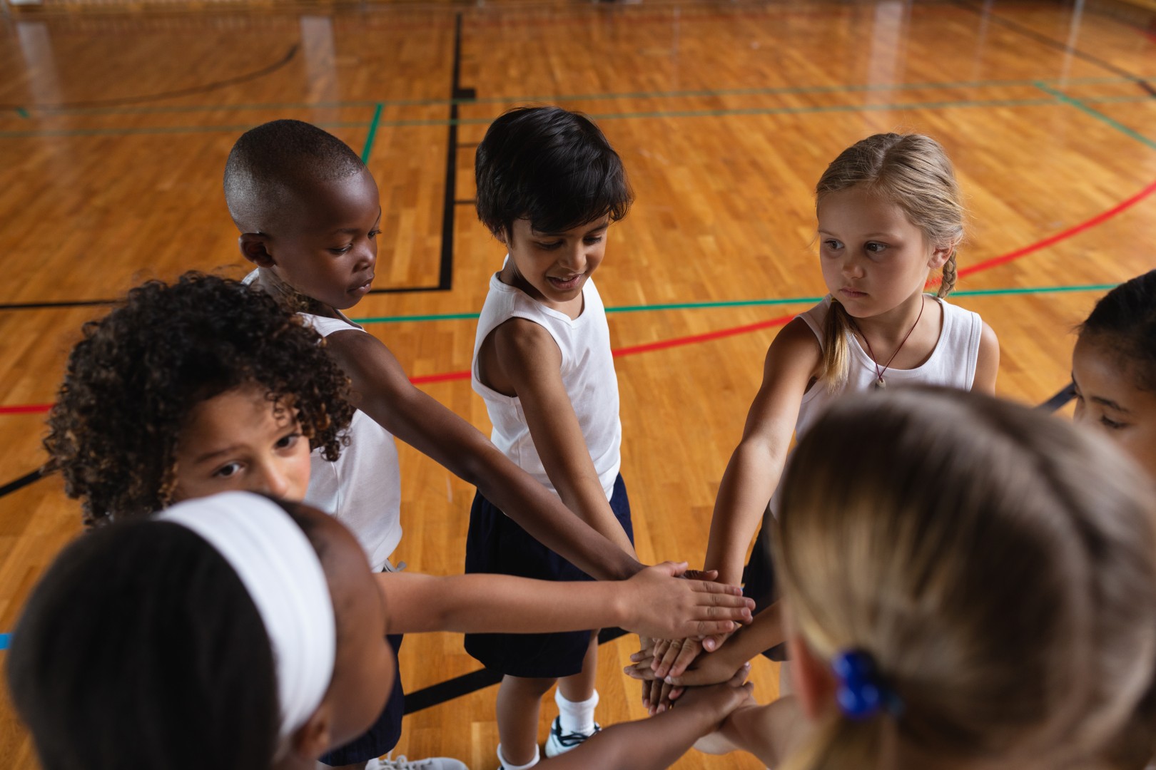 Overhead schoolkids forming hand stack at basketball court in school