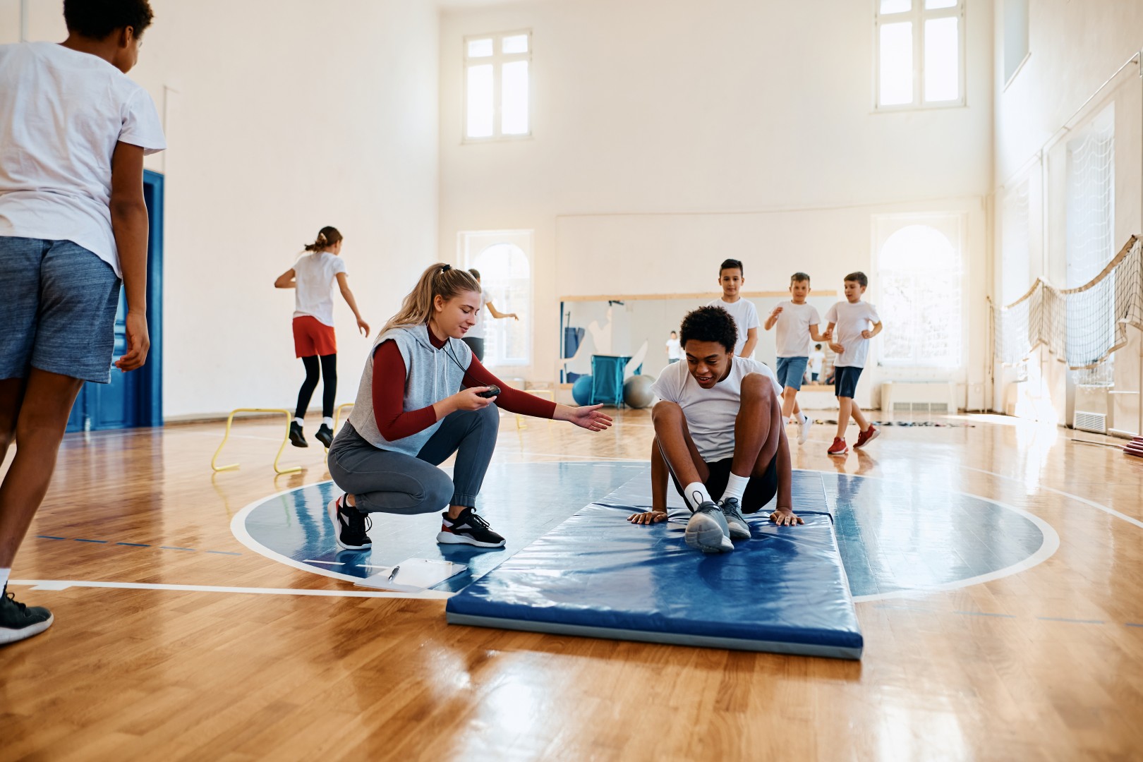 Elementary students having physical activity class with sports teacher at school gym.